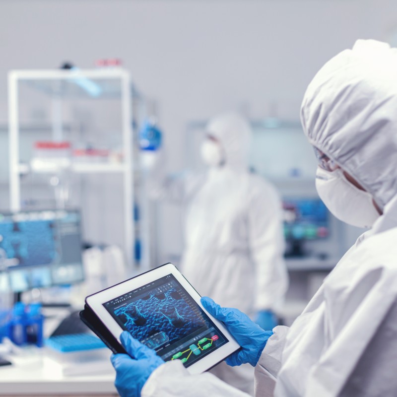 Concentrated medical researcher using digital tablet dressed protective suit against infection with coronavirus team scientists conducting vaccine development using high tech technology res